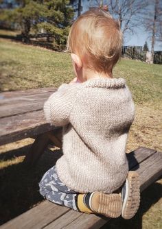 a little boy sitting on top of a wooden bench