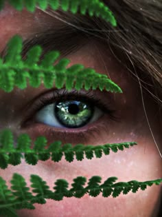 a woman's face with green leaves covering her eyes and the image of a fern behind her