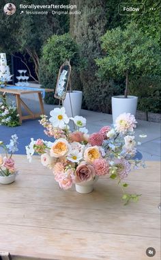 a wooden table topped with two vases filled with flowers next to each other on top of a patio