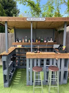 an outdoor bar made out of pallets with stools in the grass and some bottles on top