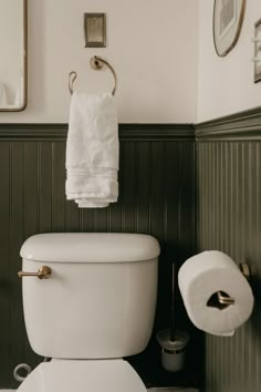 a white toilet sitting in a bathroom next to a roll of toilet paper on the wall