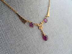 STUNNING beautiful German Made 1920s Art Deco necklace! This is a beauty with strong Art Deco design and gorgeous deep purple amethyst color glass stones.The necklace is set in gold tone setting and is marked Germany on the back. It measures about 16.5 inches in length and the centre drop is about 1.25 inches, all in wonderful like new condition-looks seldom worn, definitely gift worthy! Enjoy wearing this gorgeous Deco necklace and adding it to your collection. We combine shipping and ship inte Art Deco Jewelry For Vintage Events, Art Deco Jewelry With Vintage Charm For Vintage Events, Formal Art Deco Jewelry With Vintage Charm, Art Deco Vintage Charm Jewelry For Formal Occasions, Vintage Charm Art Deco Jewelry For Formal Occasions, Formal Art Nouveau Necklace, Art Deco Gemstone Necklace For Anniversary, Classic Amethyst Necklaces For Wedding, Yellow Gold Art Deco Jewelry For Vintage Events