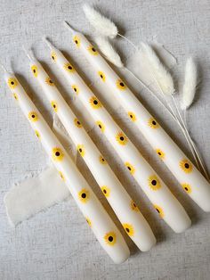 six white candles with yellow and black flowers on them sitting next to some feather feathers