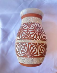 a brown and white vase sitting on top of a white cloth covered table next to a wall