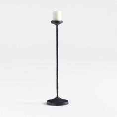 a tall black candle holder with a single white candle in it's center, on a white background