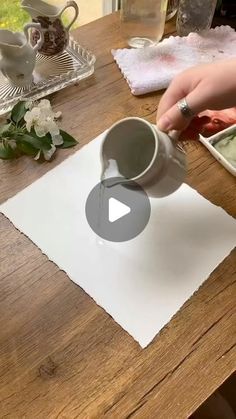 a person pouring something into a cup on top of a wooden table next to flowers