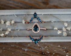 three rings with blue and white stones in a box on top of wooden table next to dried flowers