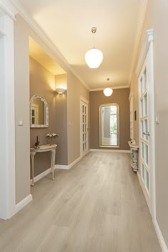 an empty hallway with white trim on the walls and wood flooring, along with two mirrors