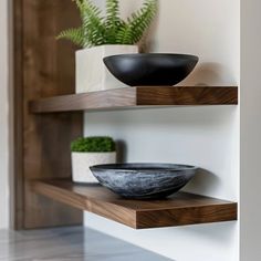 two black bowls sit on wooden shelves next to plants