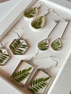 four earrings with green leaves on them sitting in a white box next to each other