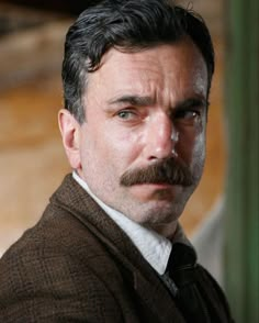 a close up of a person wearing a suit and tie with a moustache