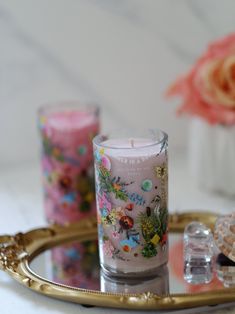 three candles sitting on top of a gold tray next to some pink flowers and shells