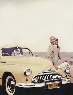 a black and white photo of a woman sitting on the hood of a vintage car