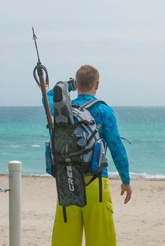 a man standing on the beach with his back to the camera, holding onto a fishing pole