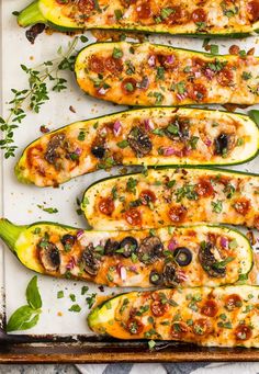 stuffed zucchini boats on a baking sheet topped with cheese and toppings, ready to go into the oven