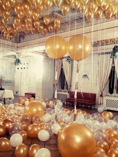 gold and white balloons floating from the ceiling in a room filled with tables and chairs