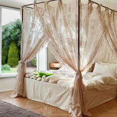 a canopy bed with curtains and pillows on top of it in front of a window