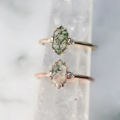 two rings sitting on top of a rock with green and white stones in the middle