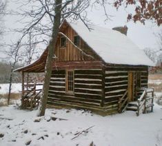 an old log cabin is covered in snow and sits next to a tree with no leaves on it