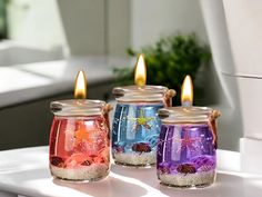 three glass jars filled with colorful sand and sea creatures sitting on top of a white table