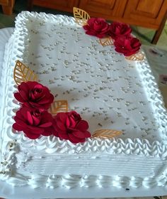 a cake with white frosting and red flowers on it's side, sitting on a table