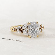 an oval diamond ring with three pear shaped diamonds on the band and side stones in yellow gold