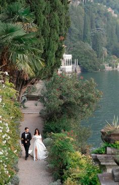 a bride and groom walking down a path by the water