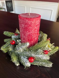 a red candle sitting on top of a wooden table next to evergreen leaves and berries