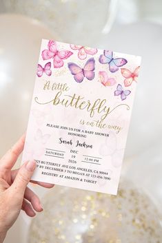 a person holding up a pink and purple butterfly birthday party card in front of balloons