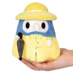 a hand holding a yellow and blue stuffed animal with a hat on it's head