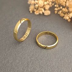 two gold wedding rings with names engraved on them and one has a heart in the middle