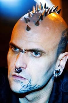 a bald man with spikes on his head and piercings around his ears is staring at the camera