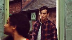 a man standing in front of a mirror wearing a plaid shirt and neck tie with his hands in his pockets