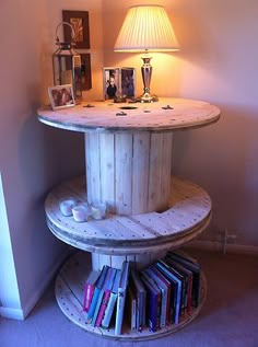 a round wooden table with books on it and a lamp in the corner next to it