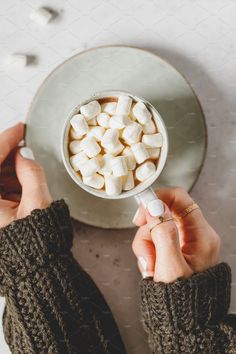 two hands holding a mug filled with marshmallows