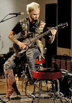 a man sitting on top of a stool while playing an electric guitar in front of a microphone