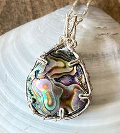 This beatiful wire wrapped Abalone shell pendant is one of my favorites, it has mesmerising swirls of rainbow colors that mimic the ocean it came from. It would make a great addition to a beach or mermaid themed outfit!  As with all my other gemstone products, the shell gemstone is guaranteed to be 100% real, natural, and undyed. This stone pendant has been wire wrapped with an intricate pattern of silver colored copper wire. The cabochon is prong set in its wire wrap, and it is additionally glu Handmade Silver-plated Wire Necklaces, Handmade Silver Plated Wire Necklaces, Wire Wrapped Silver Plated Pendant Necklace, Silver Plated Wire Wrapped Pendant Necklace, Bohemian Pendant Jewelry In Silver Plated Wire, Bohemian Silver-plated Pendant Jewelry, Bohemian Silver Plated Pendant Jewelry, Unique Hand Wrapped Silver Plated Wire Necklace, Unique Silver-plated Wire-wrapped Jewelry