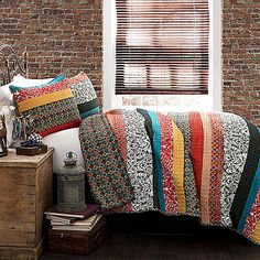 a bed sitting next to a window with a colorful blanket and pillows on top of it