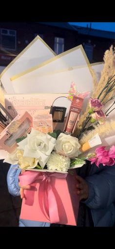 a person holding a pink gift box with flowers and books on it in front of a building