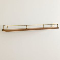 a wooden shelf with two brass bars on the top and bottom, against a white wall