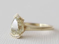 a yellow gold ring with a pear shaped diamond on the top and side stones around the band