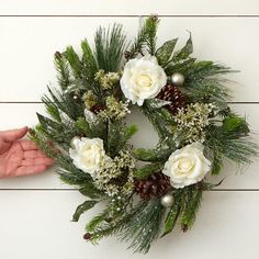 a wreath with white flowers and greenery is being held by someone's hand