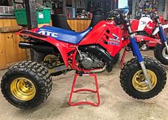 a red and blue dirt bike parked inside of a garage next to two other motorcycles