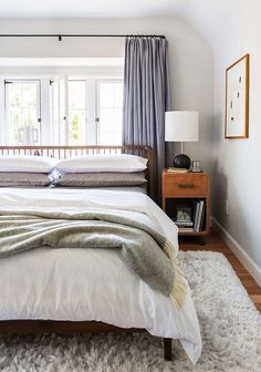 a bed sitting in a bedroom next to a window with curtains on the windowsill