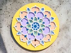 a yellow plate with a colorful flower design on the top is sitting on a concrete surface