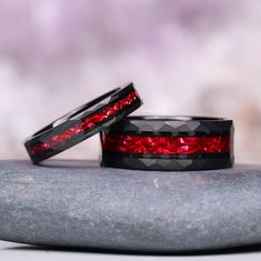 two black and red wedding bands sitting on top of each other next to a rock