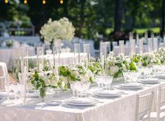 the table is set with white and green flowers, silverware, and candlesticks