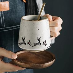 a person holding a cup with reindeer designs on it and a wooden tray underneath them