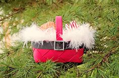 a pink basket with white feathers on it sitting in a pine tree next to other ornaments