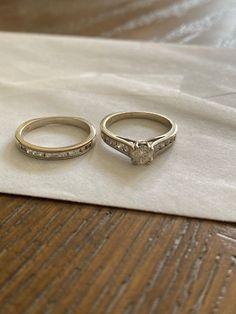 two wedding rings sitting on top of a white napkin next to each other, one with a diamond set in the middle